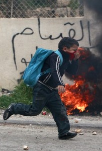 A Palestinian schoolboy runs past a burning tyre during clashes between Israeli troops and Palestinian stone-throwers in Hebron