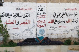 A man rests in front of a wall decorated with religious phrases written by members of al Qaeda's Nusra Front in Aleppo's Qadi Askar neighborhood, Syria July 13, 2015. REUTERS/Abdalrhman Ismail
